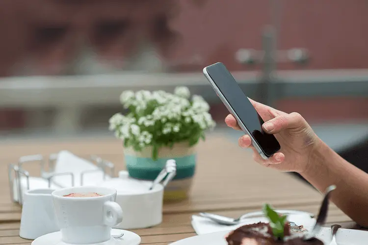 Smartphone screen showing a social feed held at a café table
