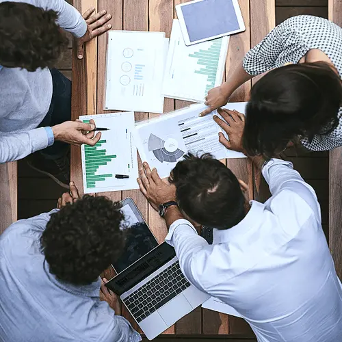 Overhead view of a team discussing charts and data around a table with a laptop