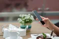Smartphone screen showing a social feed held at a café table